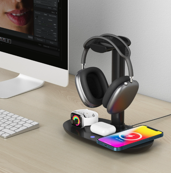 Schwarzer 4-in-1 Wireless Charging Stand mit Over-Ear-Kopfhörern, Smartphone, AirPods und Smartwatch auf einem modernen Schreibtisch neben einem Desktop-Computer